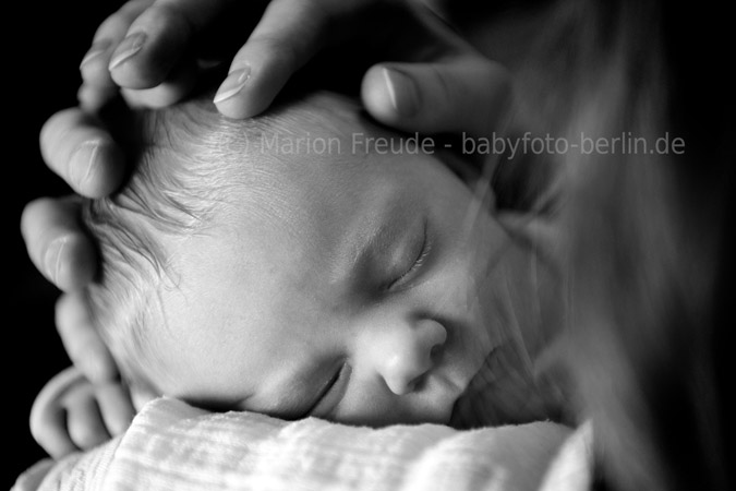 Neugeborenes mit den schützenden Händen der ELtern auf dem Kopf