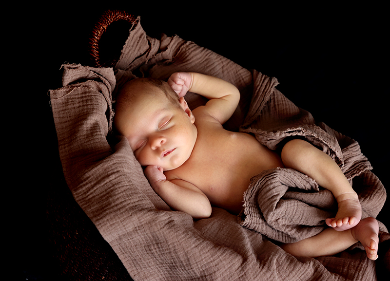 Baby liegt in einem Weidenkörbchen. Auf einer Decke.